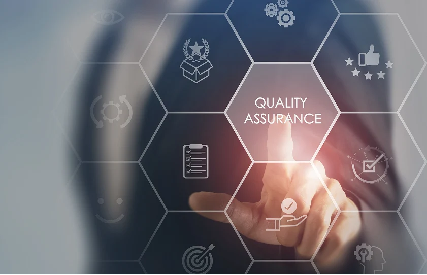 A person’s hand touches a digital interface labeled Quality Assurance, surrounded by various icons representing quality metrics and reviews.
