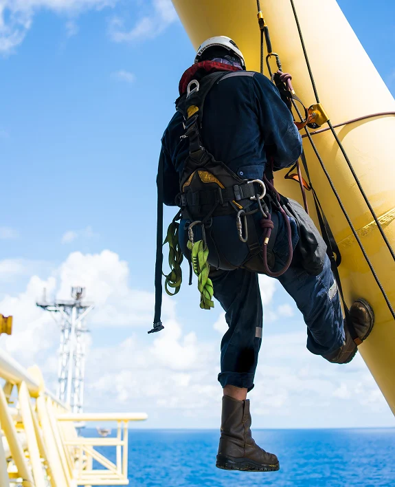 A worker in safety gear rappels down a yellow structure against a backdrop of blue sky and ocean.